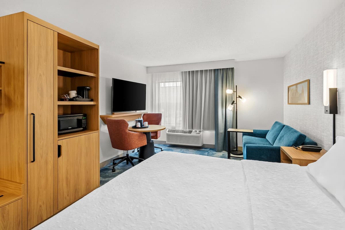 Una habitación de hotel con una cama, un escritorio con televisor de pantalla plana, un armario de madera, un sofá azul y una mesita pequeña.