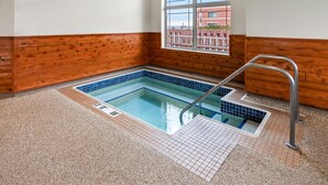 Una piscina interior pequeña con una escalera de metal, paredes de madera y un ventanal con vistas a edificios.