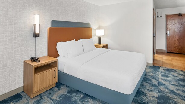 A hotel room with a bed, nightstands, a lamp, a wooden cabinet, and a door.