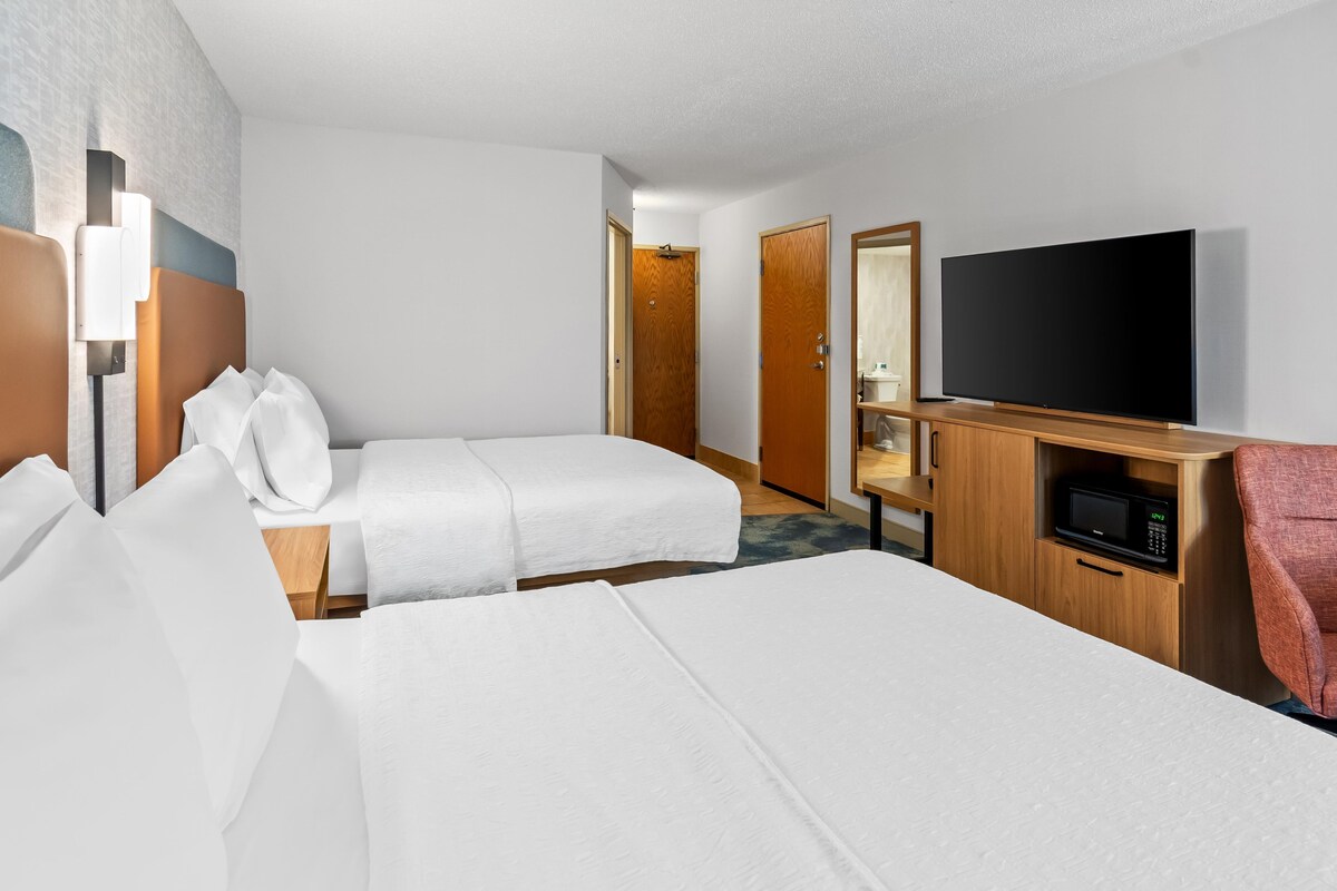 A hotel room with two beds, a TV, a microwave, and a wooden cabinet.