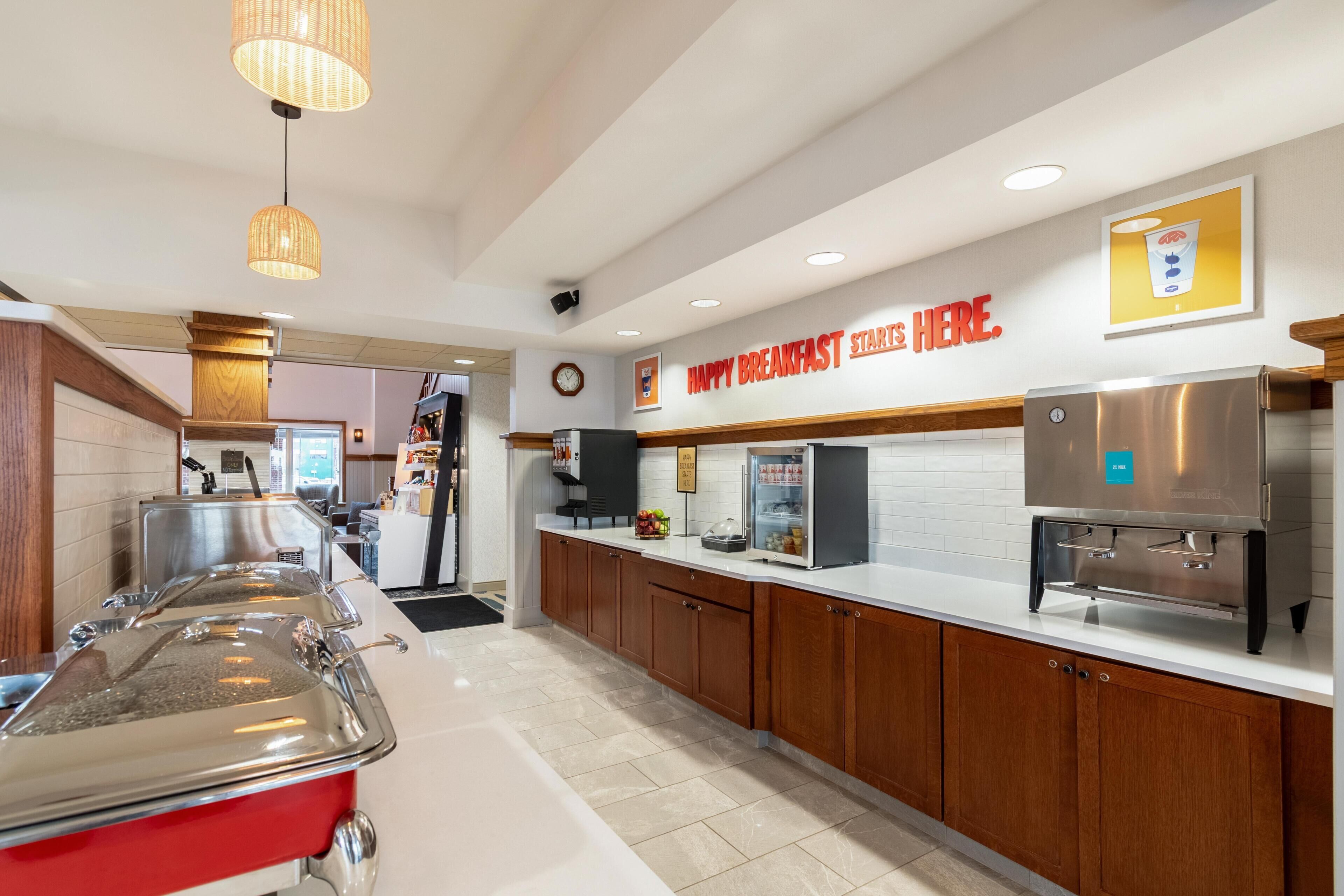 A breakfast area with a counter, buffet setup, and a sign that reads 'HAPPY BREAKFAST START HERE.'