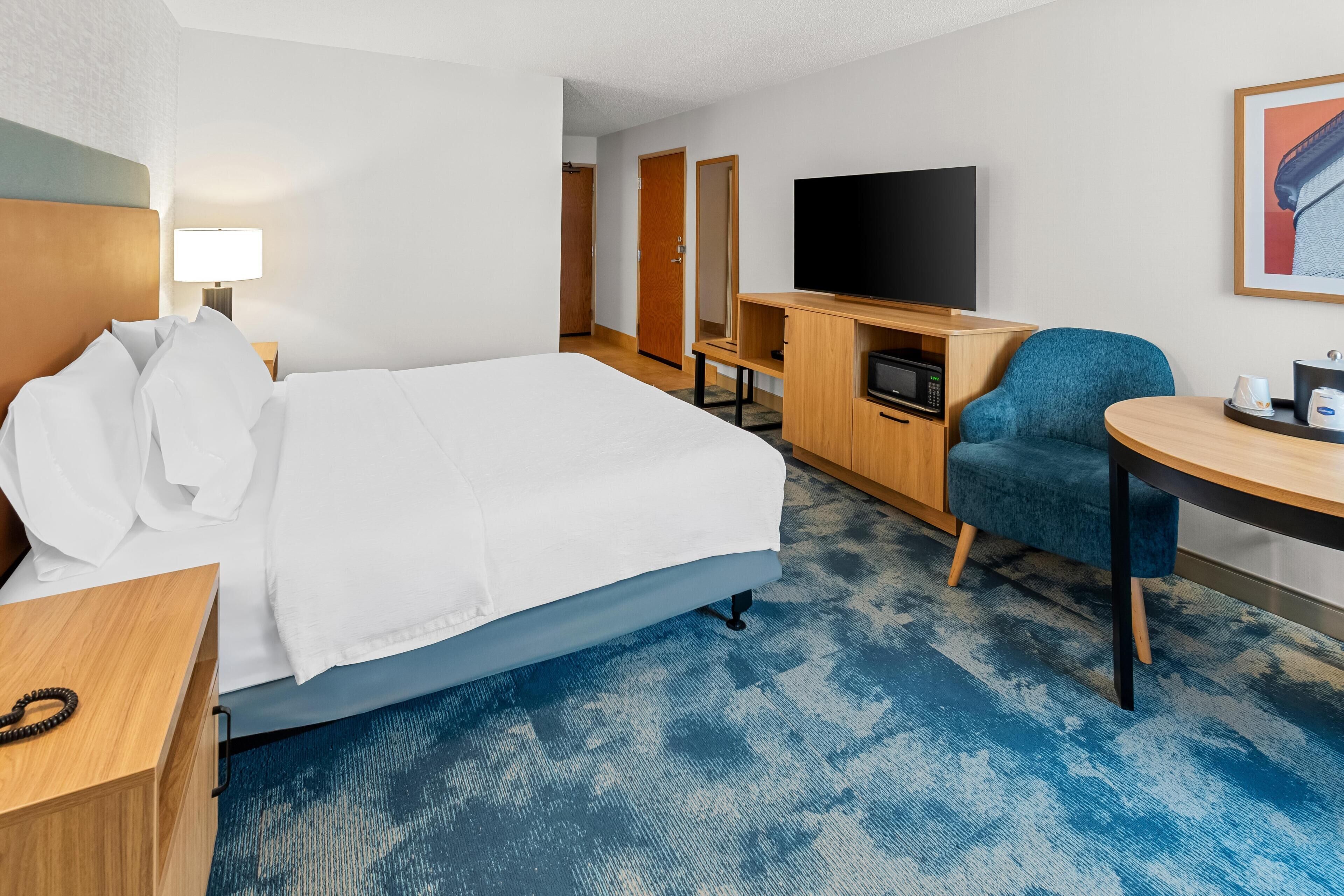 A hotel room with a bed, a desk, a TV, a chair, and a small table.