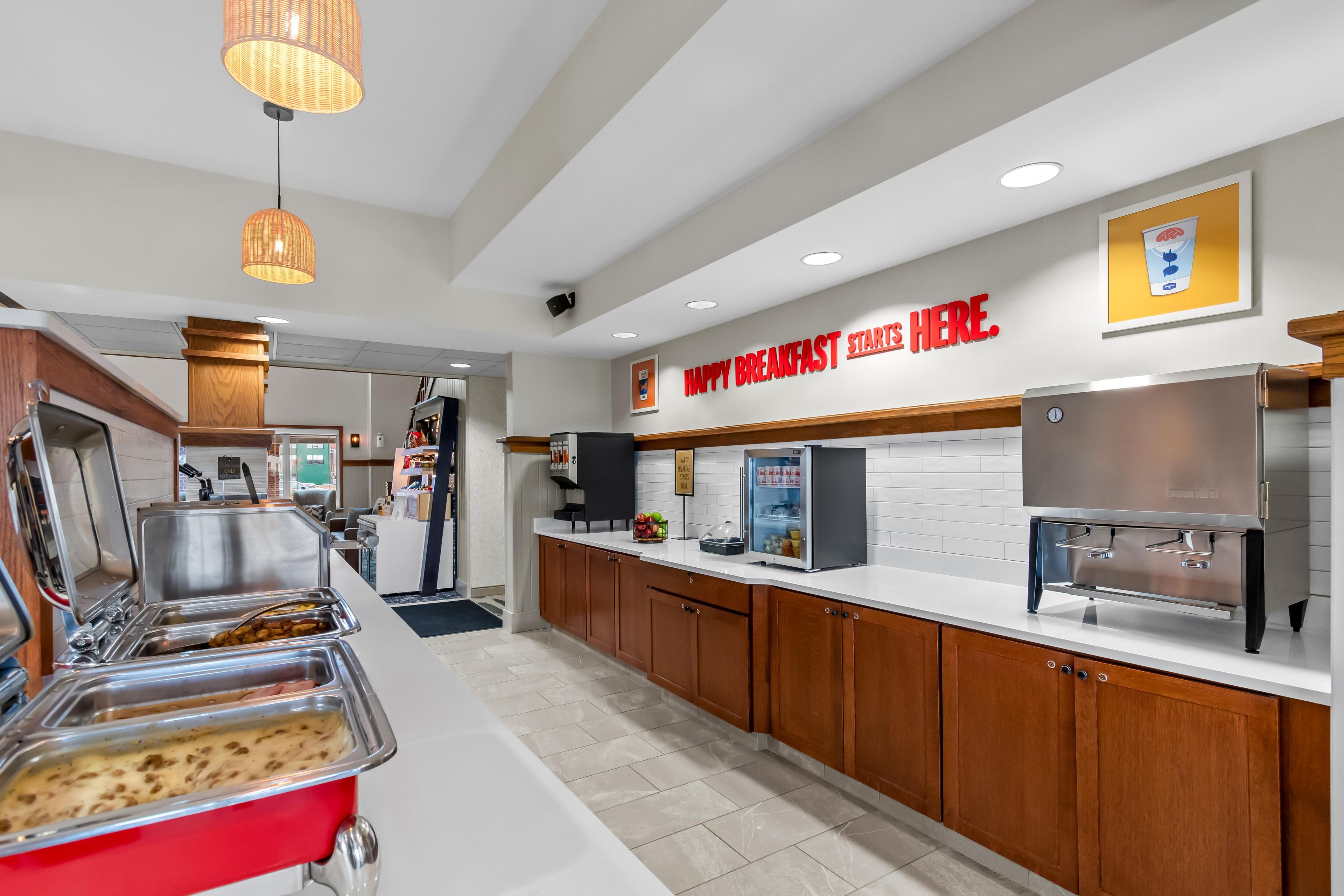 Un área de desayuno con servicio de buffet, una cafetera y un letrero que dice 'HAPPY BREAKFAST STARTS HERE'.