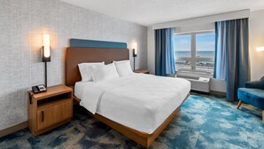 Een hotelkamer met een groot bed, bedlampen, een nachtkastje, uitzicht op zee en een blauwe stoel.