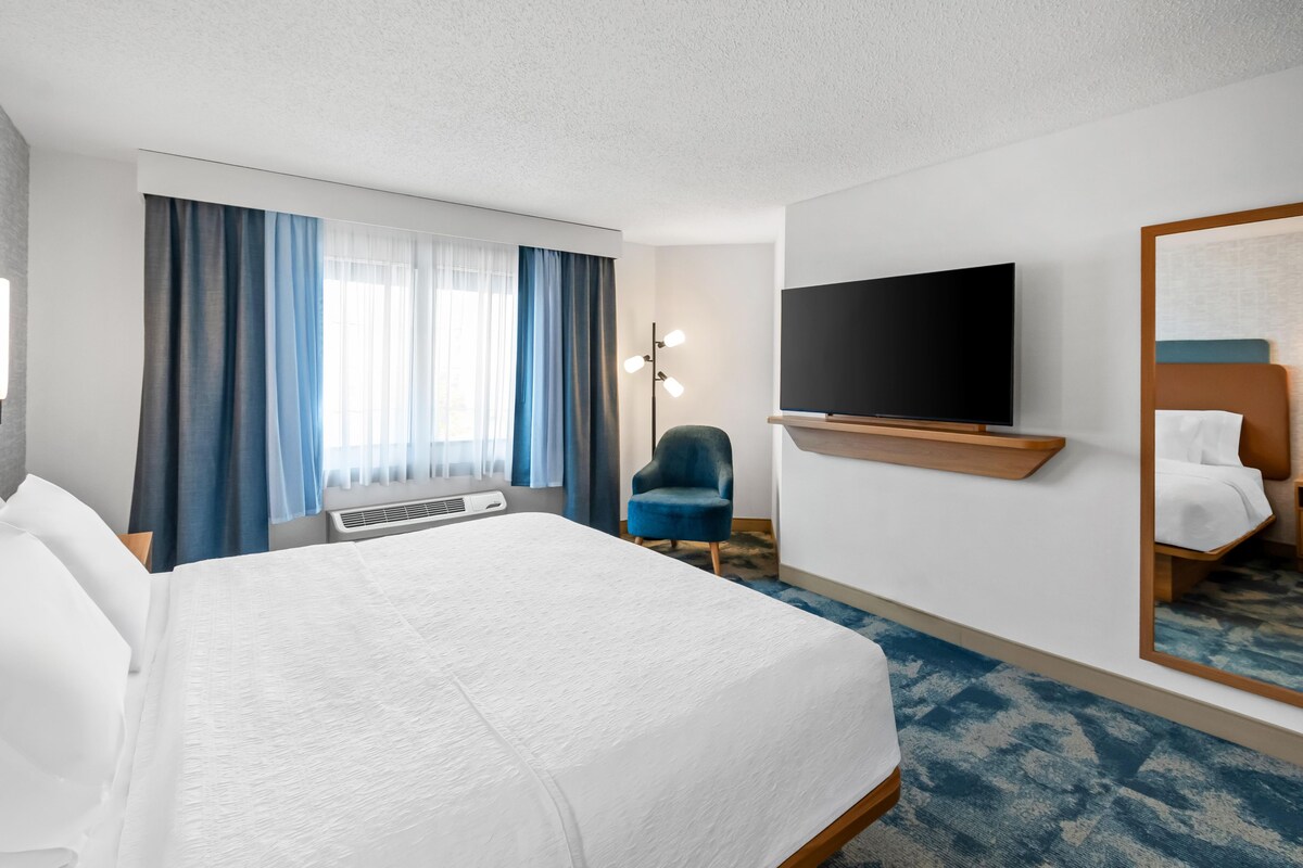 A hotel room with a large bed, a flat-screen TV, a chair, and a mirror.