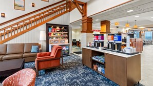 Een hotel lobby met een trap, zithoek en een koffiehoek.