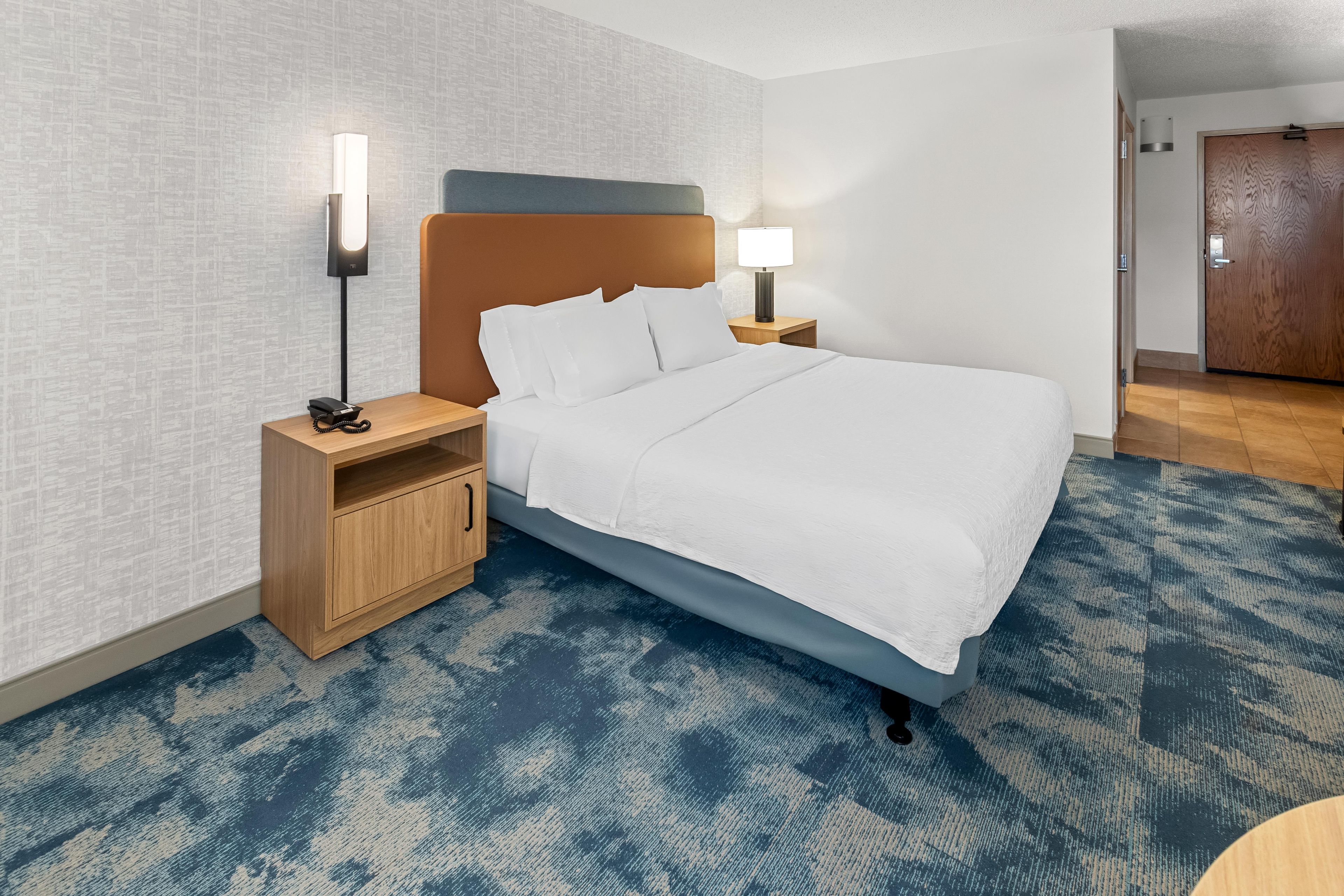 A hotel room with a bed, two bedside tables, a nightstand, a wooden wardrobe, and a door.