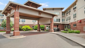 A multi-story building with a covered entrance area, brick pillars, and a clear sky.