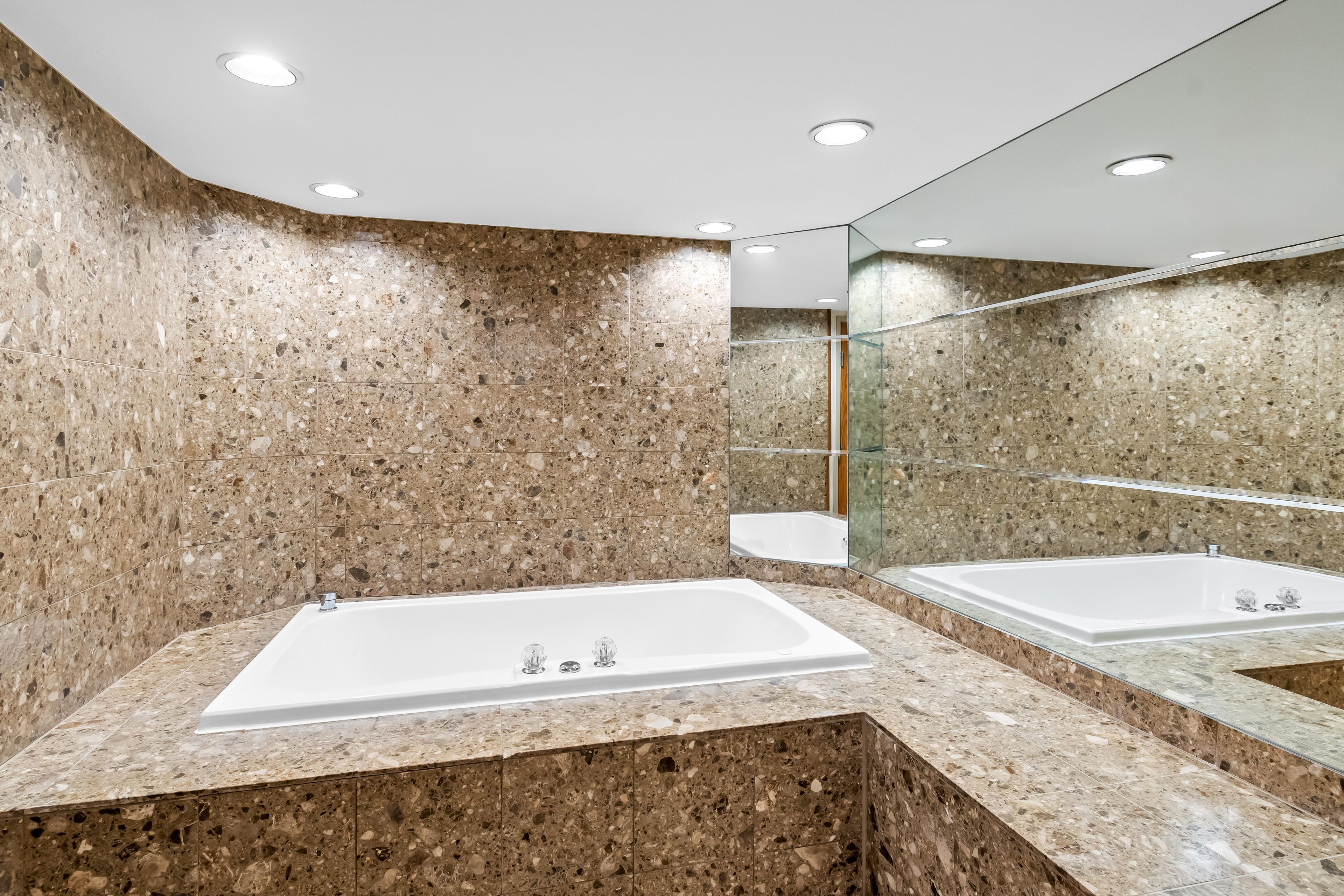 Un baño moderno con una bañera rectangular grande, encimeras de granito y una pared espejada.