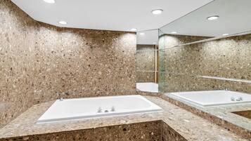 Un baño moderno con una bañera rectangular grande, encimeras de granito y una pared espejada.