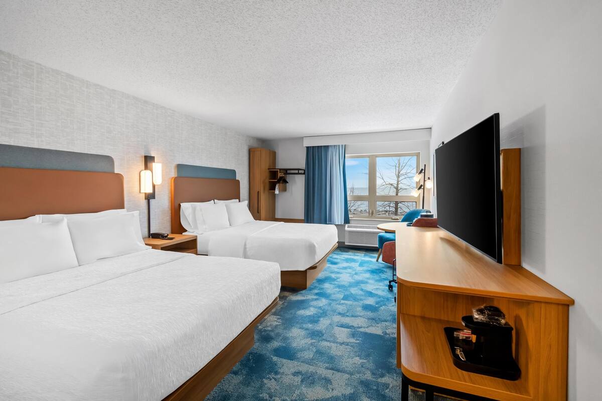 A hotel room with two beds, a desk, a TV, and a window with a view.