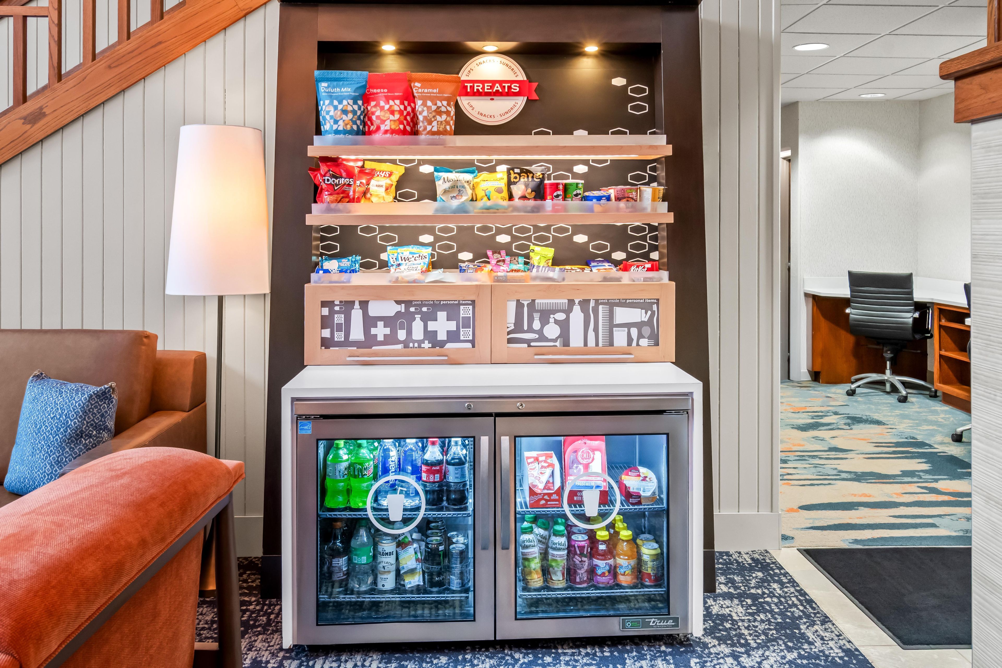 A vending machine with snacks and drinks, a sofa with a pillow, and a desk with a chair.