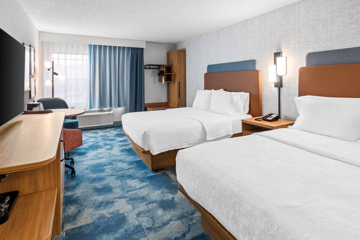 A hotel room with two beds, a desk, a chair, a wardrobe, and a window with curtains.
