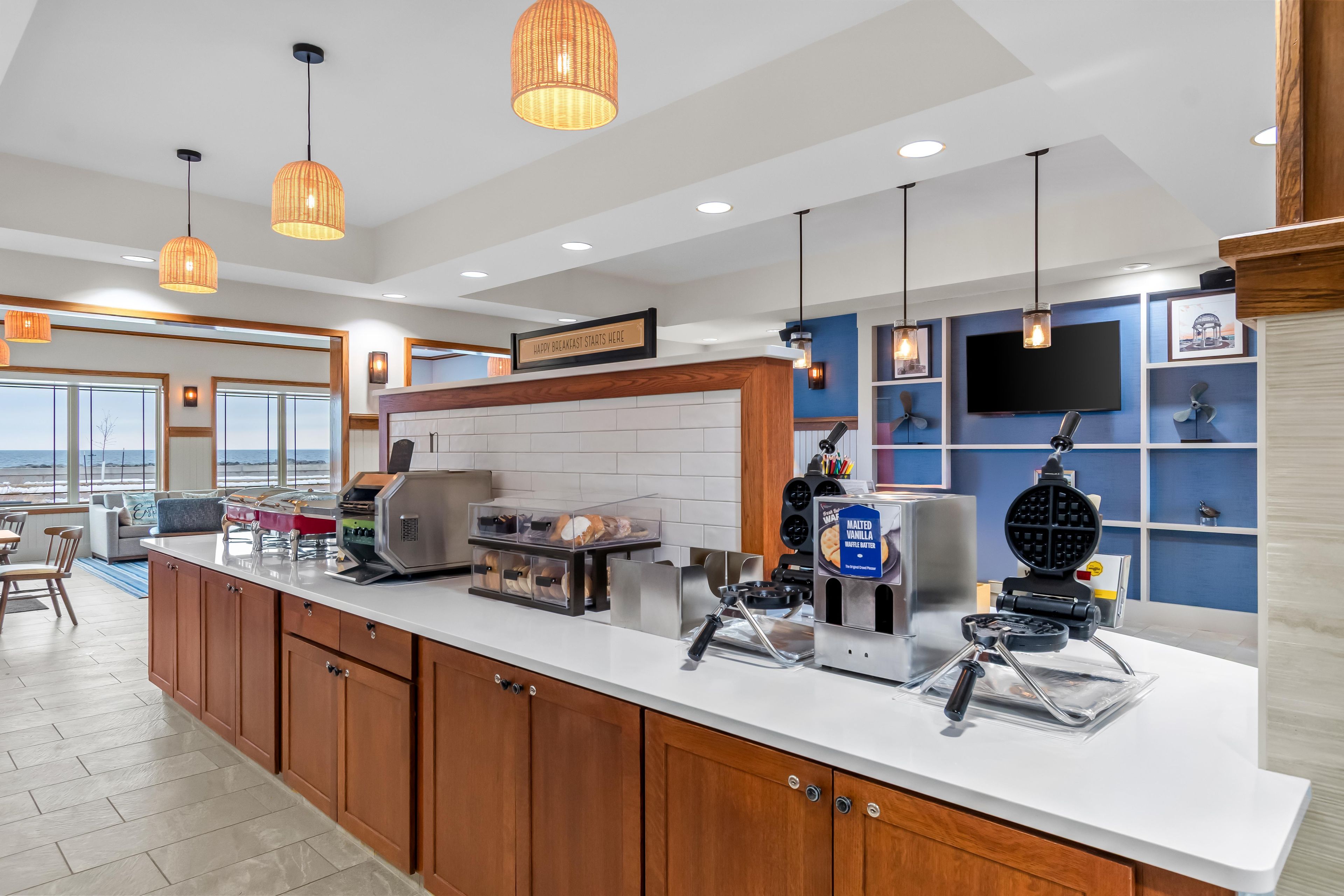 A modern kitchen with a breakfast bar, waffle maker, and coffee station.