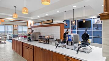 A modern kitchen with a breakfast bar, waffle maker, and coffee station.