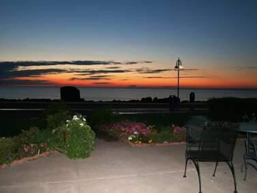 A patio with a view of the sunset over the ocean, a metal chair, and a table.