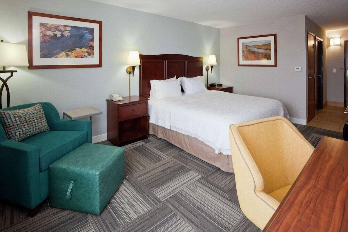 Una habitación de hotel con cama, sofá verde, mesita de noche de madera, una pequeña mesa y una silla.