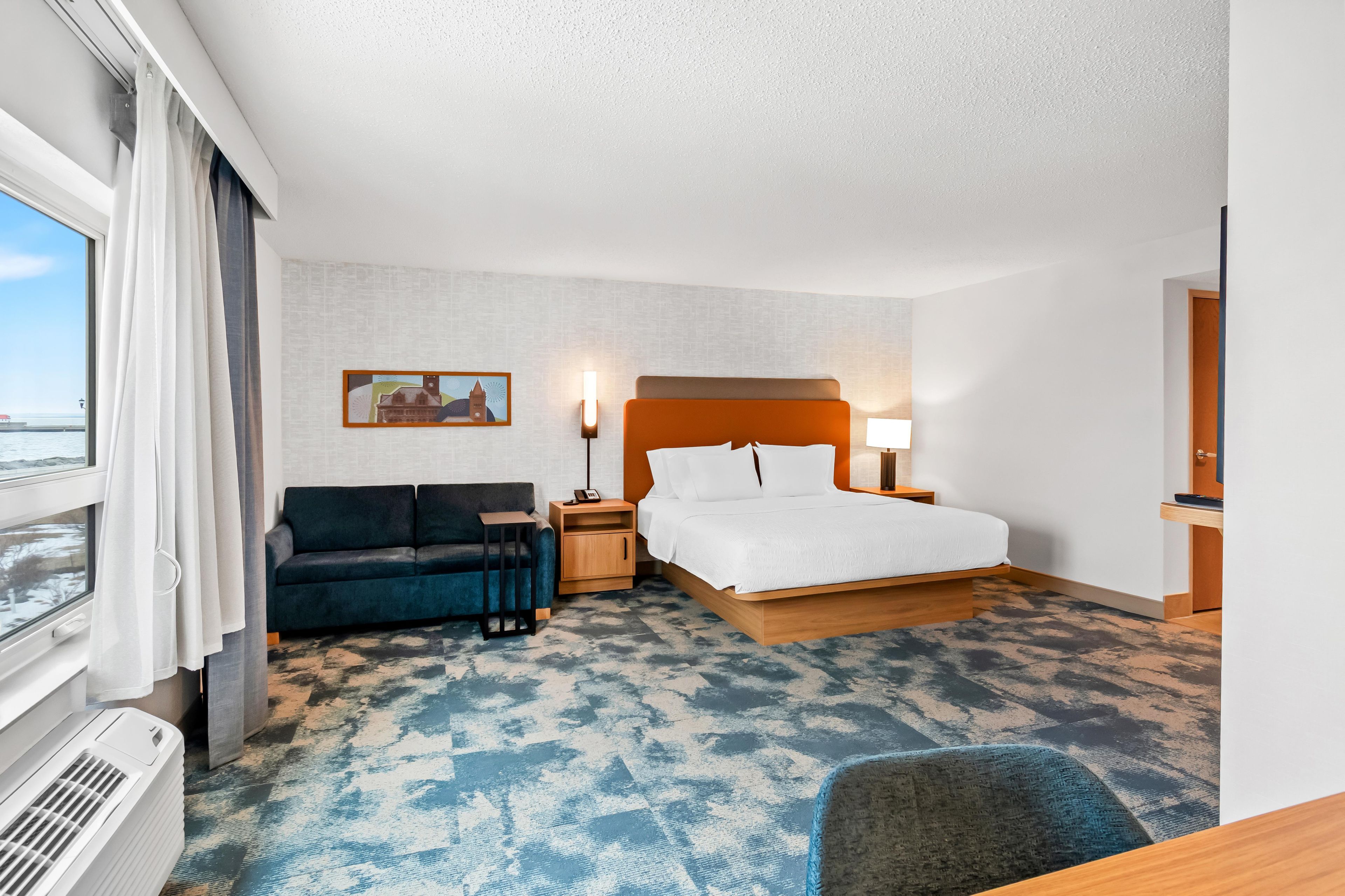 A hotel room with a bed, a sofa, a desk, and a view of the sea.