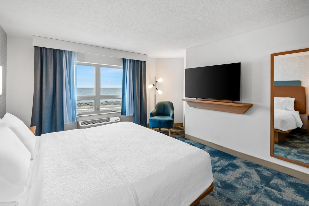 Habitación de hotel con una cama grande, televisión de pantalla plana, una silla y vista al océano.