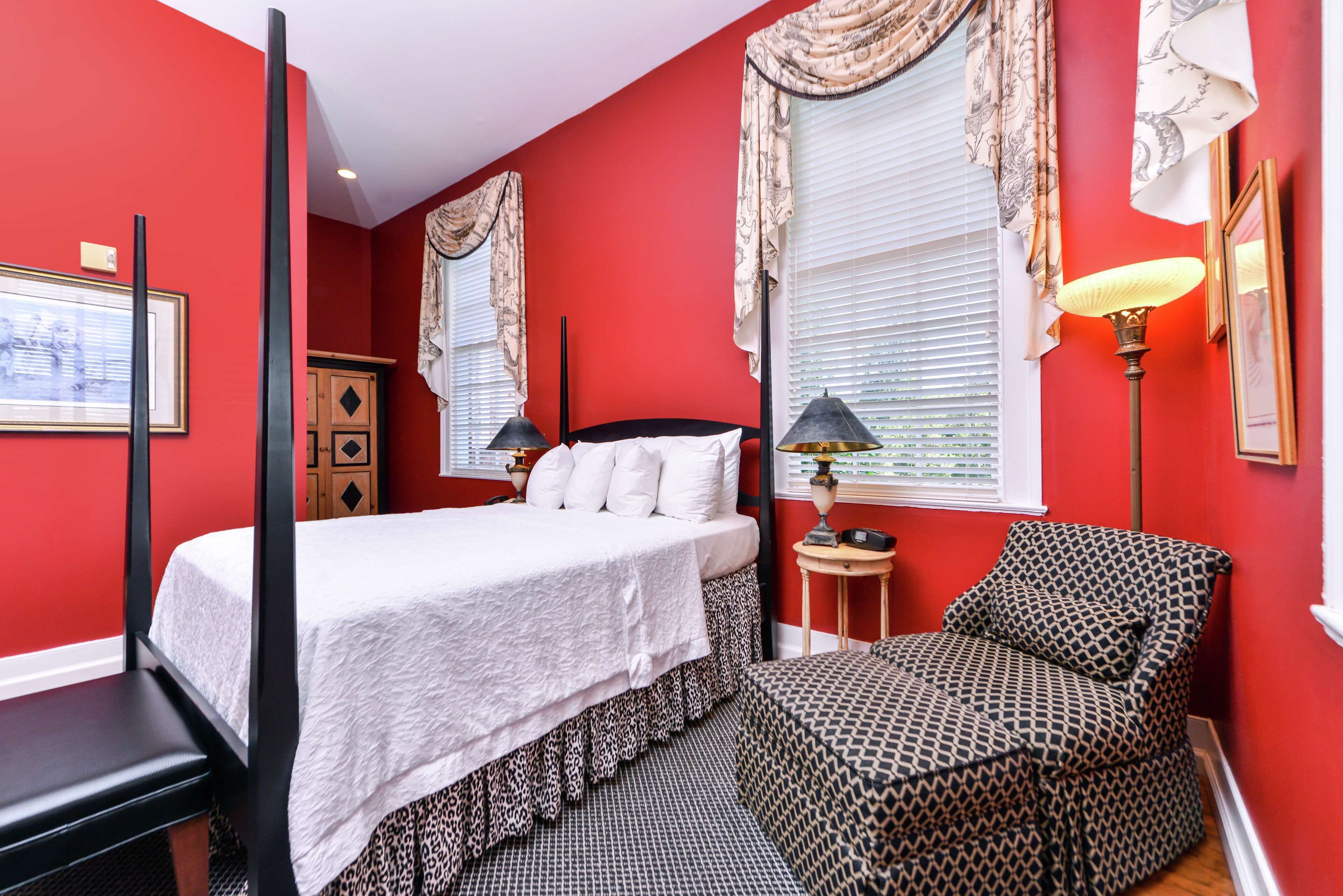 A four-poster bed with white linens, a patterned armchair, and a small bedside table with a lamp.