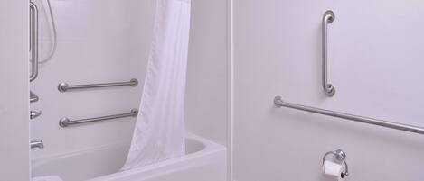 Ein Badezimmer mit Badewanne, Toilette und Duschbereich. Es sind Haltegriffe und ein Handtuchhalter vorhanden.