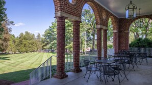 A covered patio with brick columns, outdoor tables and chairs, and a view of a well-manicured lawn. - Hampton Inn Lexington-Historic District (Lexington)