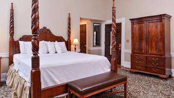 A four-poster bed with a bench, a wooden cabinet, and a patterned carpet in a hotel room.