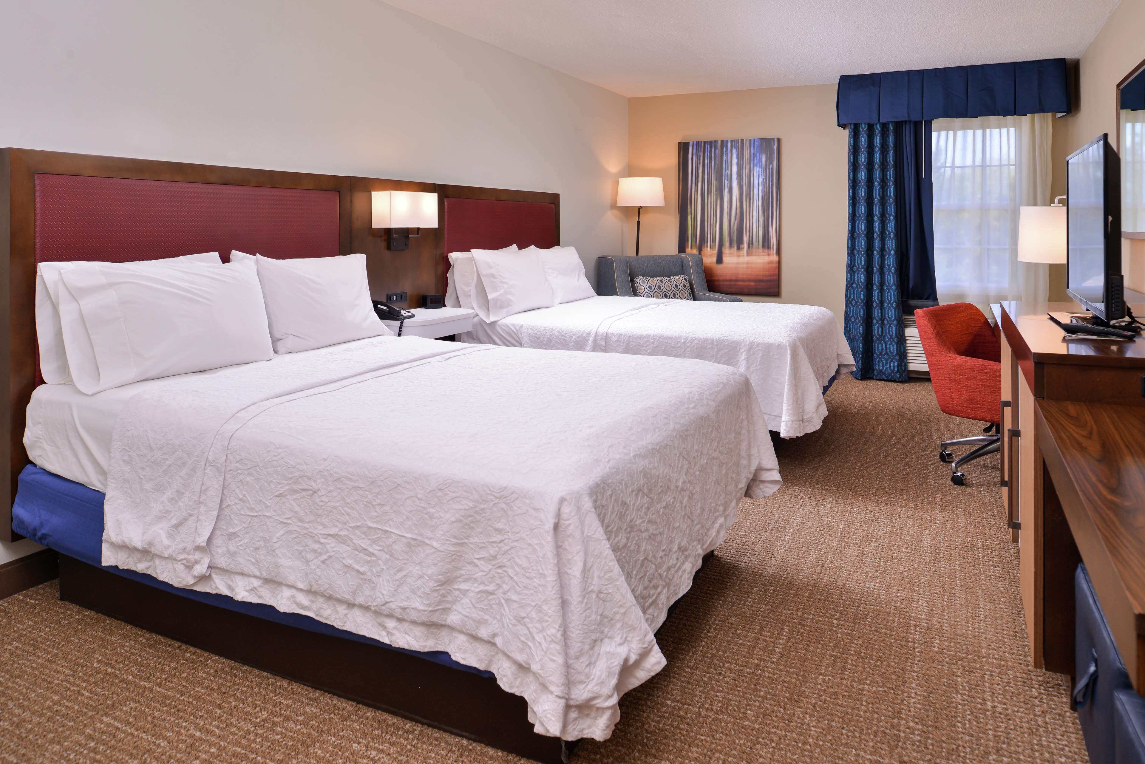 A hotel room with two beds, a desk with a computer, a chair, and a TV.