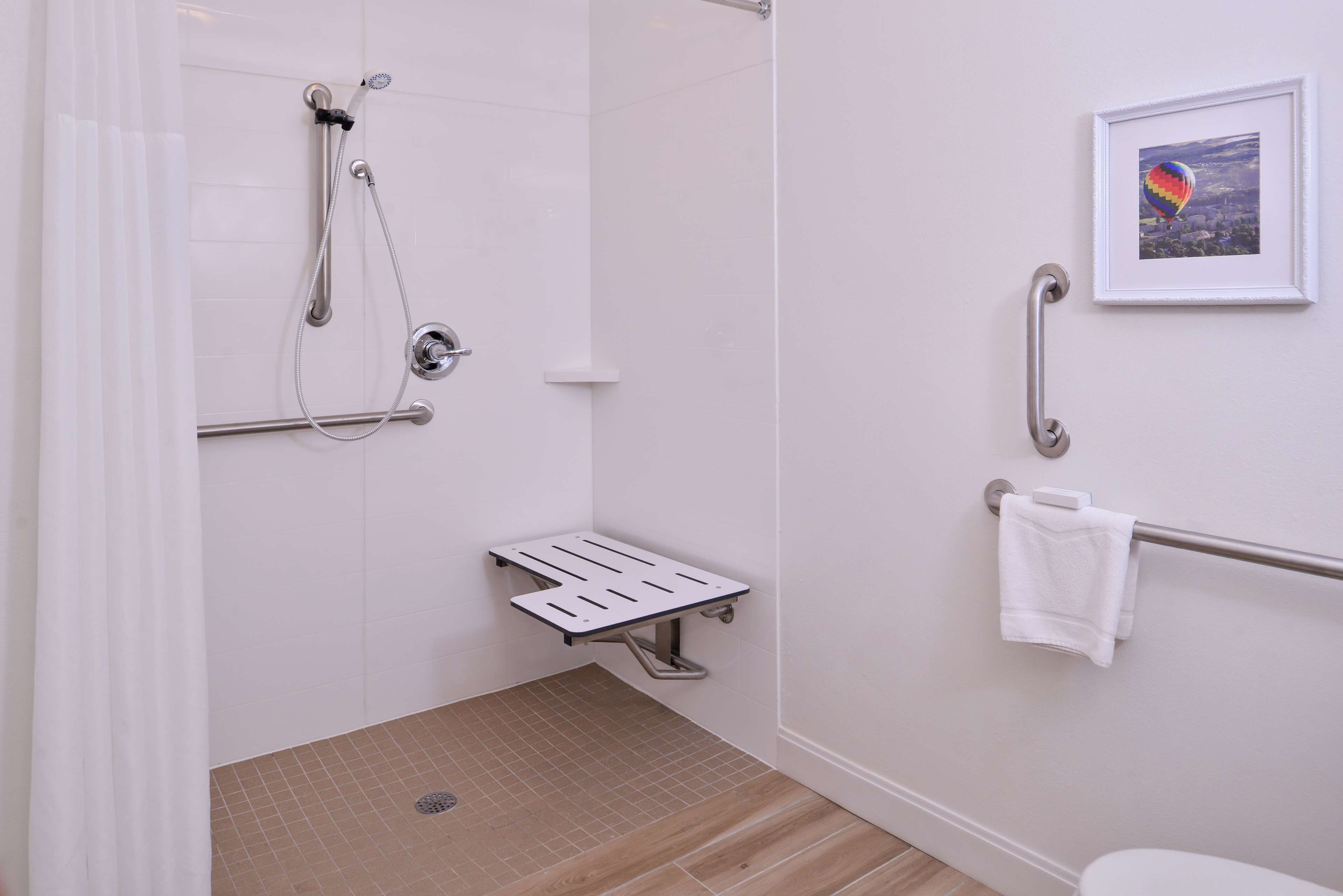 A bathroom with a shower, grab bar, and a towel rack.