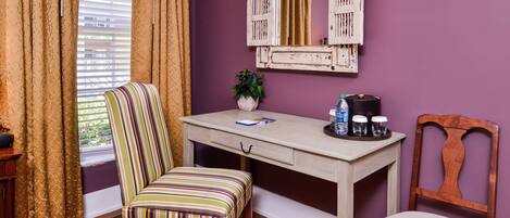 A room with a wooden desk, two chairs, a potted plant, and a decorative mirror on the wall.