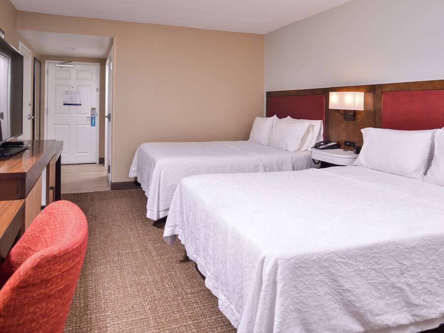 A hotel room with two beds, a desk, a chair, and a television.