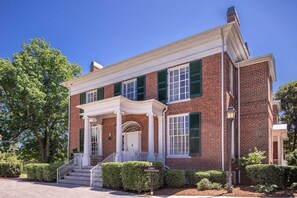 A two-story brick building with a white porch, green shutters, and a sign indicating a lobby registration area.