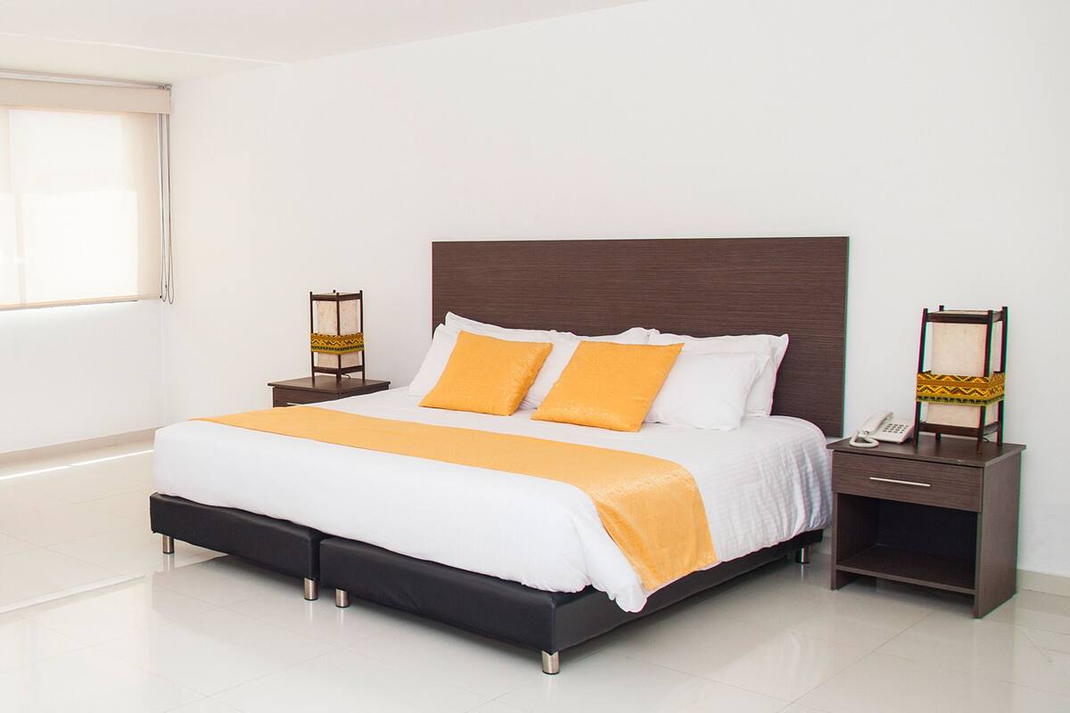 Quarto moderno com uma cama grande, duas mesas de cabeceira e uma mesinha de apoio com abajur.