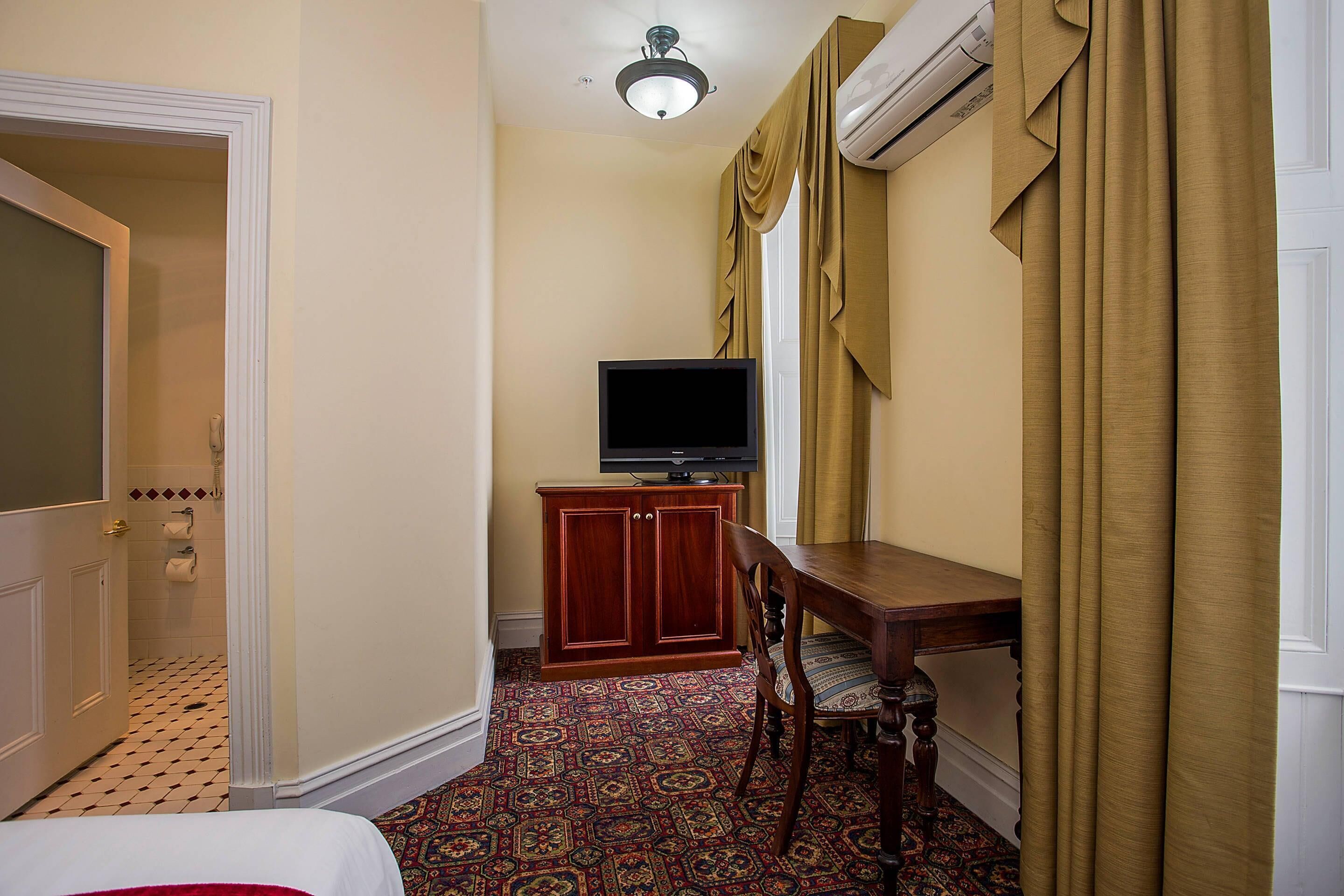 A hotel room with a bed, a desk with a television, a cabinet, and patterned carpet.
