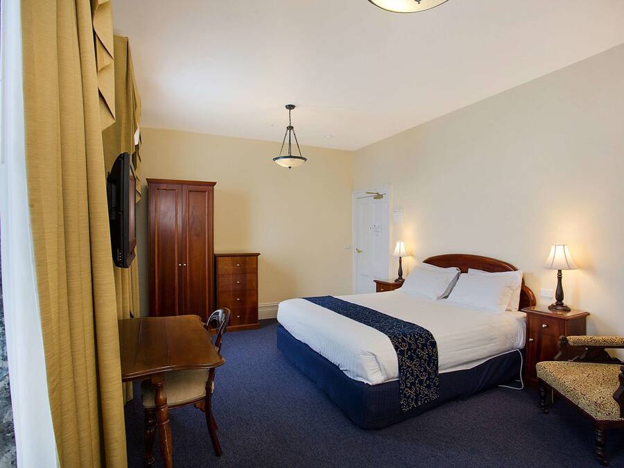 A hotel room with a bed, desk, chair, wardrobe, and a door.