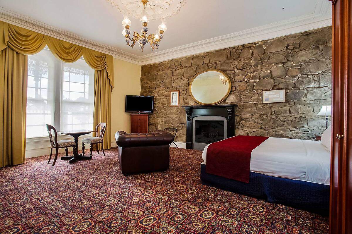 A hotel room with a stone wall, a fireplace, a bed, a television, and a dining area with a table and chairs.