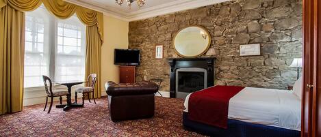 A hotel room with a stone wall, a fireplace, a bed, a television, and a dining area with a table and chairs.