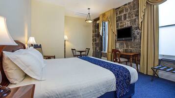 A hotel room with a large bed, a desk, a chair, a television, and a stone wall.