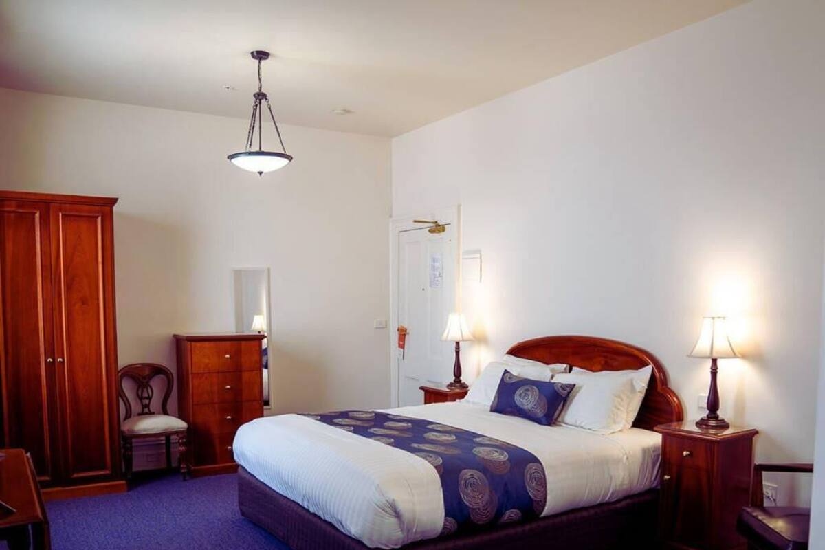 A bedroom with a large bed, wooden wardrobe, and a desk.