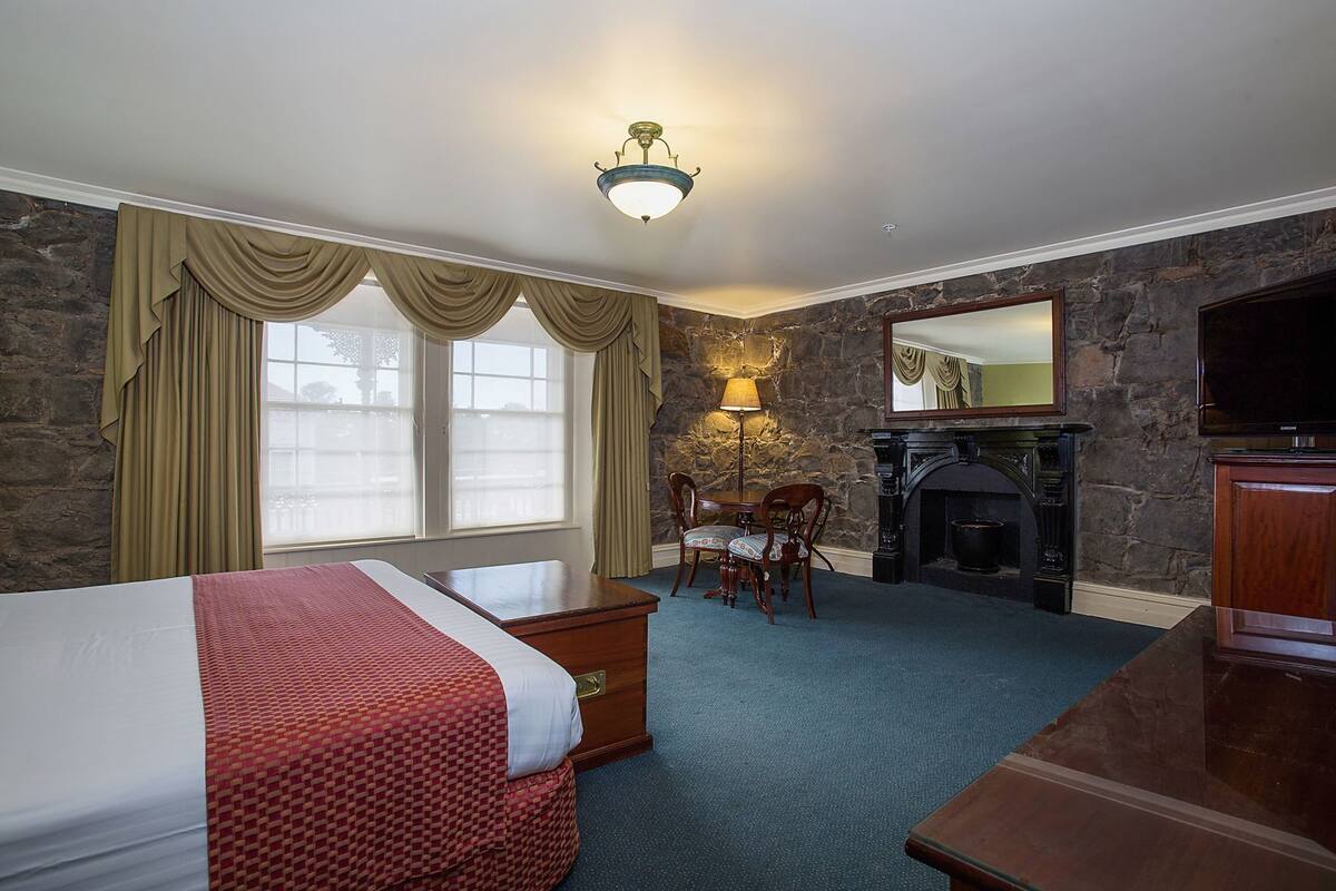 A hotel room with a bed, a desk, a chair, a fireplace, and a television.