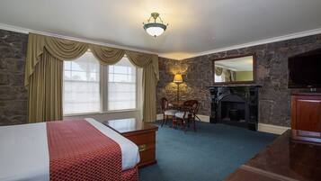 Une chambre d’hôtel avec un grand lit, un bureau, une chaise, un mur en pierre, une cheminée et un téléviseur.