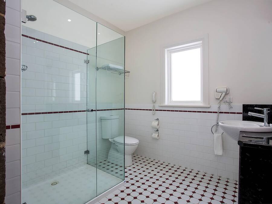 A bathroom with a glass shower enclosure, a toilet, a sink with a towel, and a window.