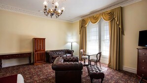 Una habitación con alfombra estampada, un sofá, una silla, una lámpara, un televisor y un ventanal con cortinas.