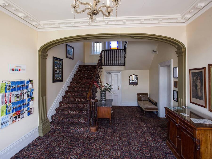 A grand staircase with ornate carpet and a chandelier, leading to a private door.