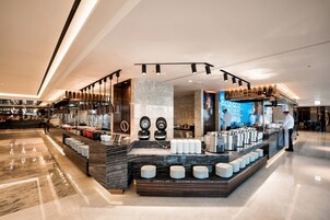Un moderno vestíbulo de hotel con un mostrador de recepción de mármol, una estación de café y una gran pantalla digital que muestra información.