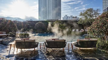 Piscina en la azotea con vapor ascendiendo, rodeada de sillones de descanso y macetas con plantas.