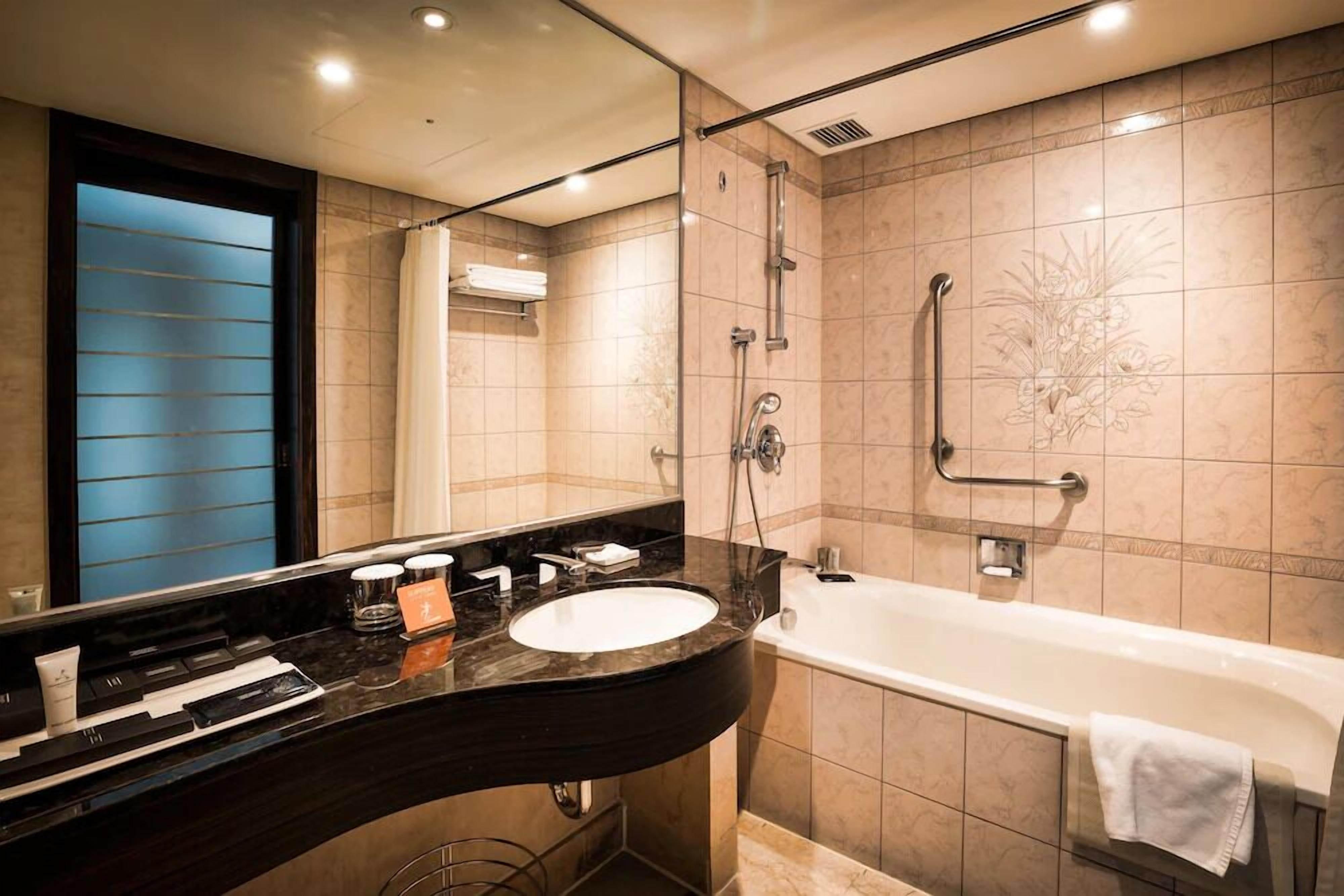 A modern bathroom with a curved black sink, a white bathtub, and a glass-enclosed shower area.