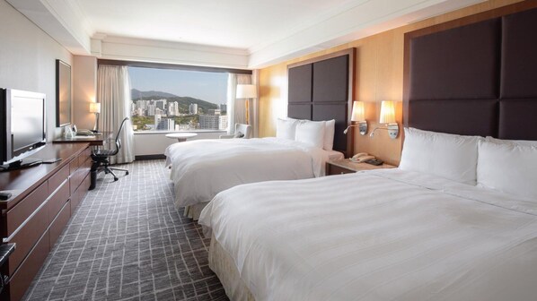 A hotel room with two beds, a desk with a chair, a TV, and a city view.