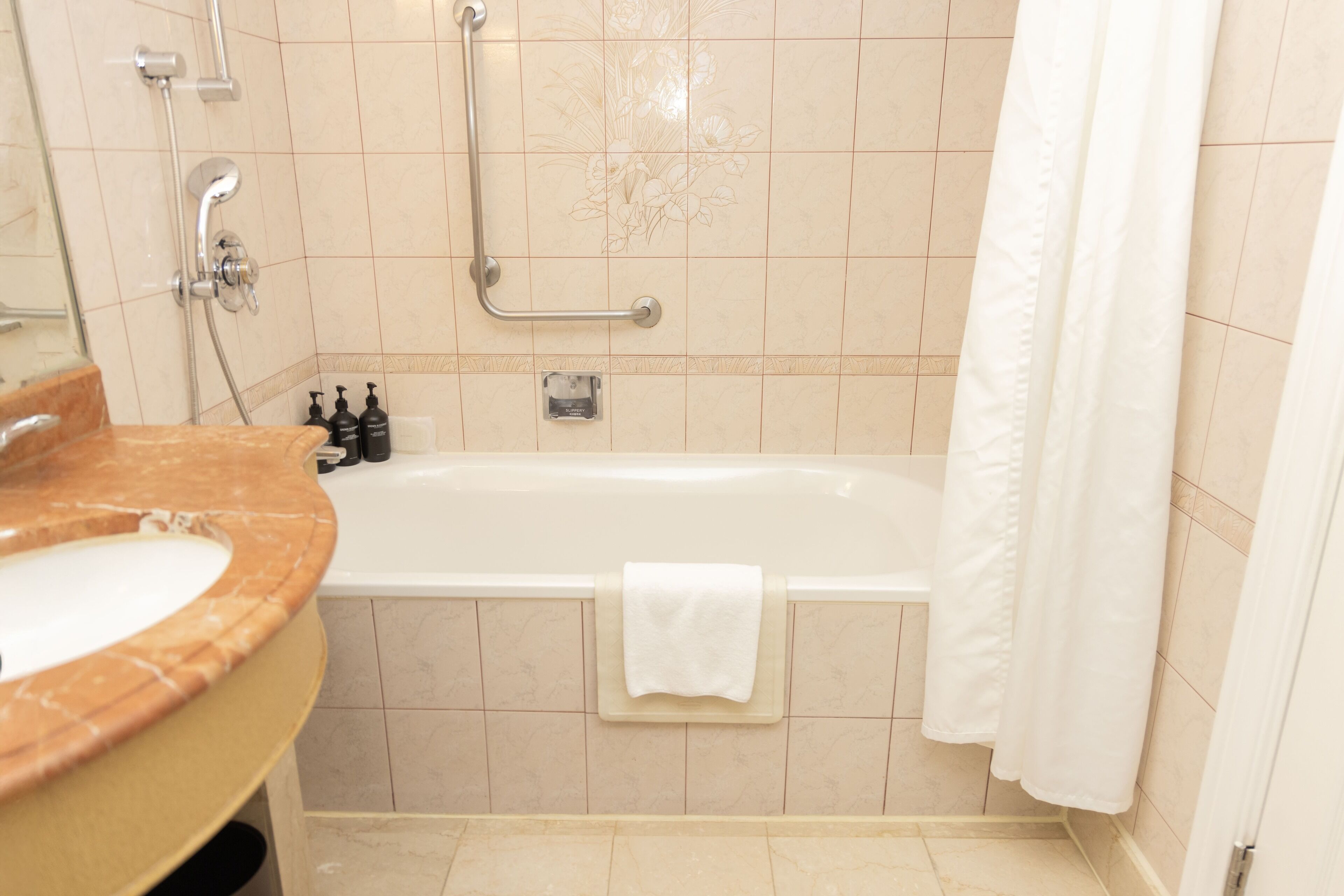 A bathroom with a bathtub, a sink with a marble countertop, and a shower with a grab bar.