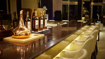 A bar area with bottles of liquor, a large wine decanter, and white cushioned chairs.